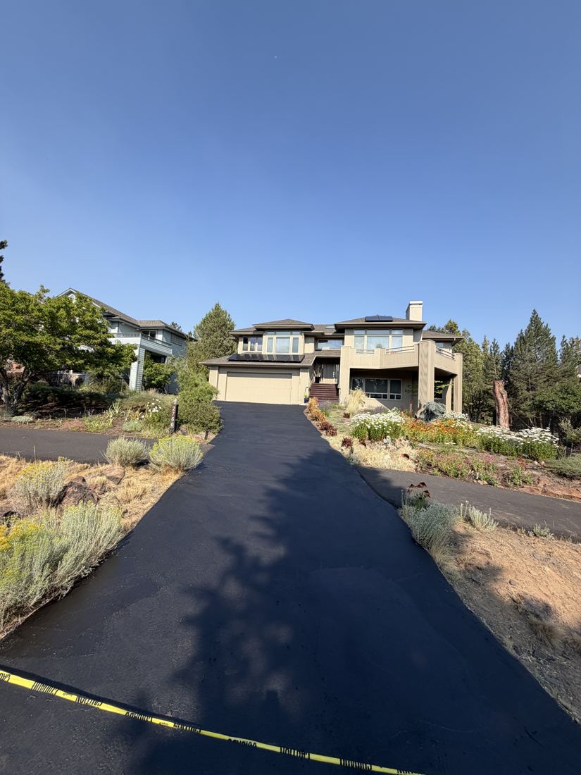 Freshly sealcoated black driveway leading up to a two-story home, taped off while it cures